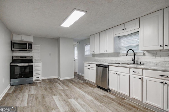 kitchen with light wood-style flooring, a sink, white cabinetry, appliances with stainless steel finishes, and decorative backsplash