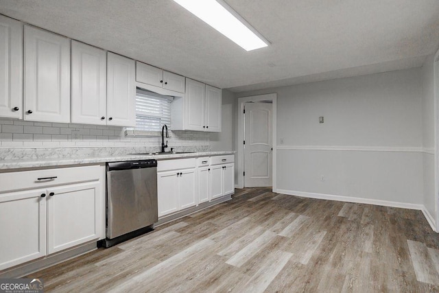 kitchen featuring light countertops, stainless steel dishwasher, a sink, and white cabinets