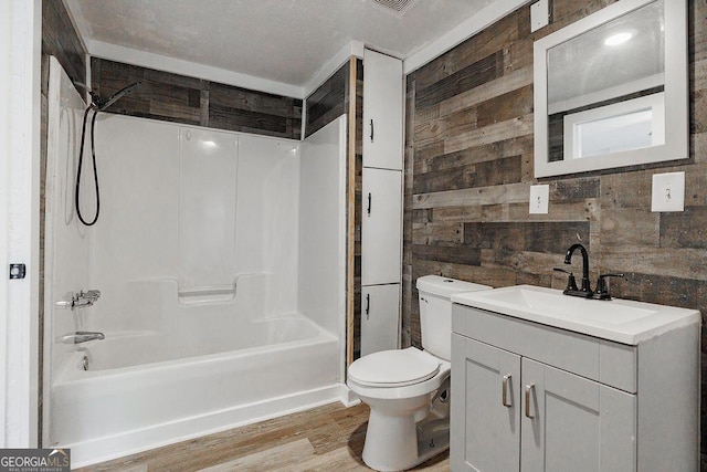 bathroom featuring toilet, wooden walls, wood finished floors, vanity, and  shower combination