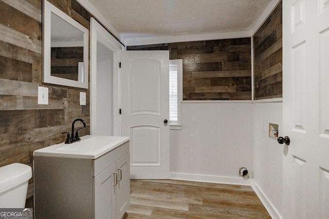 half bath with toilet, wood finished floors, vanity, and wooden walls