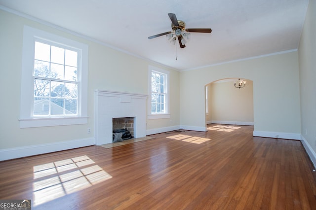 unfurnished living room with baseboards, arched walkways, wood finished floors, crown molding, and a fireplace