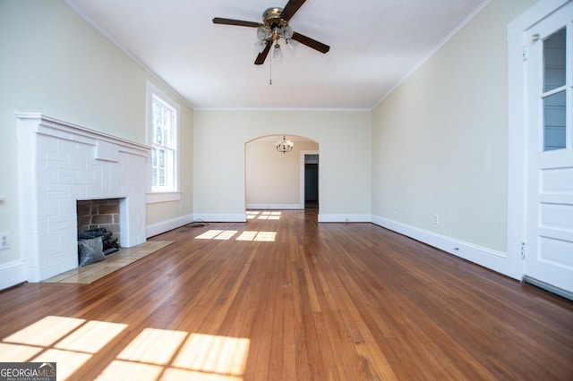 unfurnished living room with ornamental molding, arched walkways, a brick fireplace, and wood-type flooring