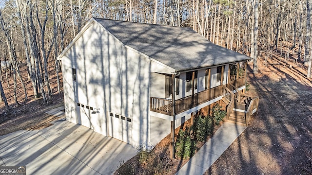 exterior space with a porch, concrete driveway, an attached garage, and stairs