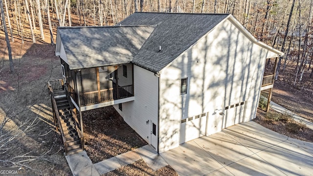 view of outbuilding featuring a garage, a sunroom, stairs, and concrete driveway