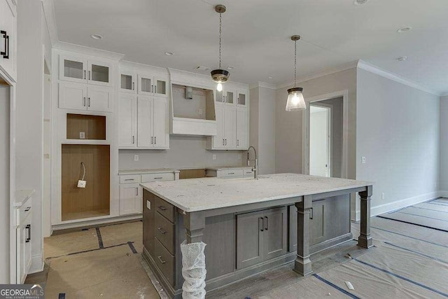 kitchen with a sink, white cabinetry, light stone countertops, an island with sink, and glass insert cabinets