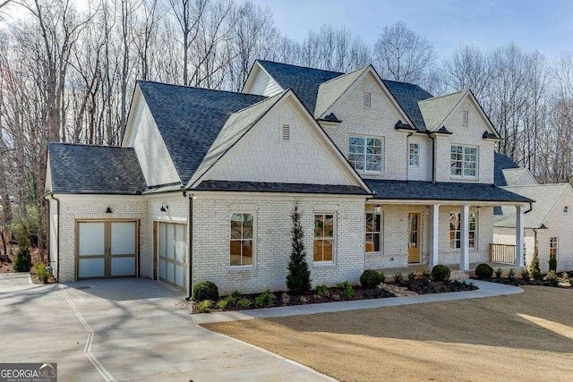 view of front of house featuring driveway, a garage, roof with shingles, covered porch, and brick siding