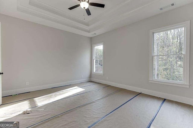 empty room featuring baseboards, visible vents, a ceiling fan, a tray ceiling, and crown molding