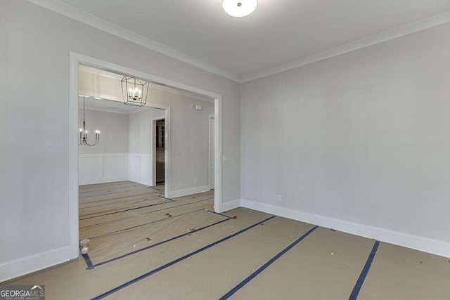 spare room featuring a chandelier, a decorative wall, a wainscoted wall, baseboards, and crown molding