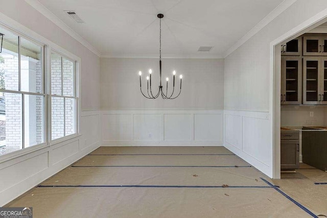 unfurnished dining area with a wainscoted wall, crown molding, visible vents, and an inviting chandelier