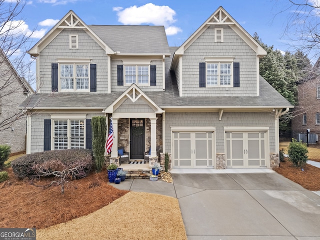 craftsman house featuring driveway, stone siding, a shingled roof, and a garage