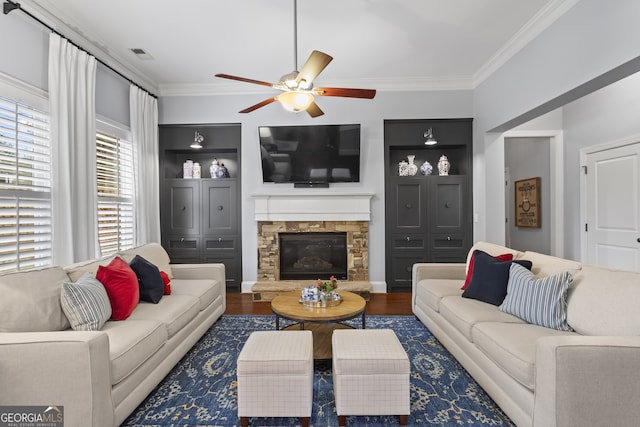 living area featuring built in shelves, visible vents, ornamental molding, a stone fireplace, and wood finished floors