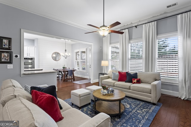 living area with visible vents, ornamental molding, wood finished floors, baseboards, and ceiling fan with notable chandelier