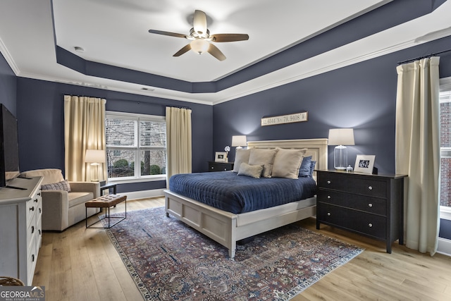 bedroom with light wood-style floors, a raised ceiling, crown molding, and a ceiling fan