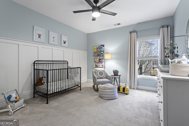 bedroom featuring a nursery area, light colored carpet, visible vents, and a decorative wall