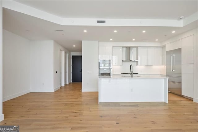 kitchen with visible vents, a sink, white cabinetry, wall chimney exhaust hood, and light wood-type flooring