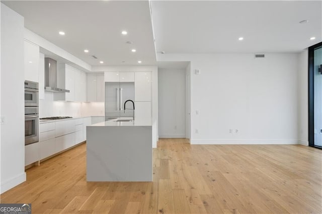 kitchen with modern cabinets, a sink, white cabinetry, light wood-style floors, and wall chimney range hood