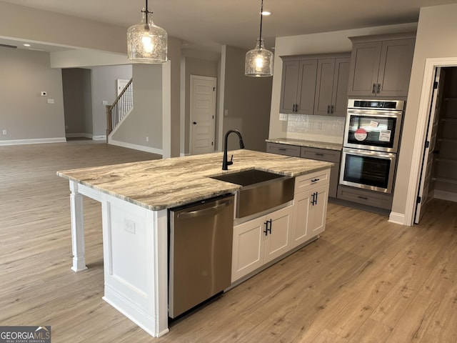 kitchen featuring a kitchen island with sink, stainless steel appliances, a sink, light wood-style floors, and backsplash