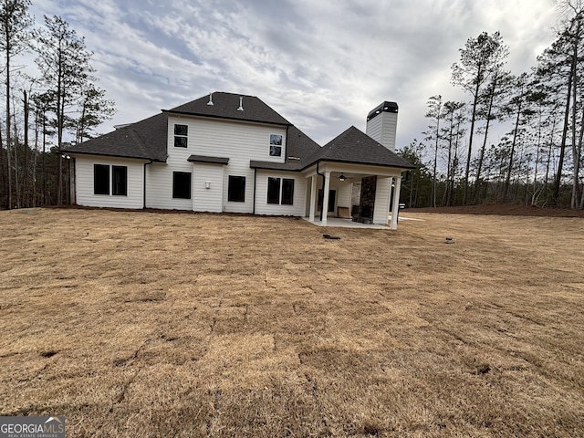 rear view of property featuring ceiling fan, a shingled roof, a yard, a chimney, and a patio area