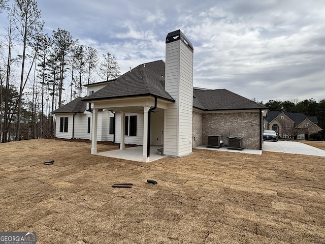 rear view of property with roof with shingles, a chimney, cooling unit, and a patio