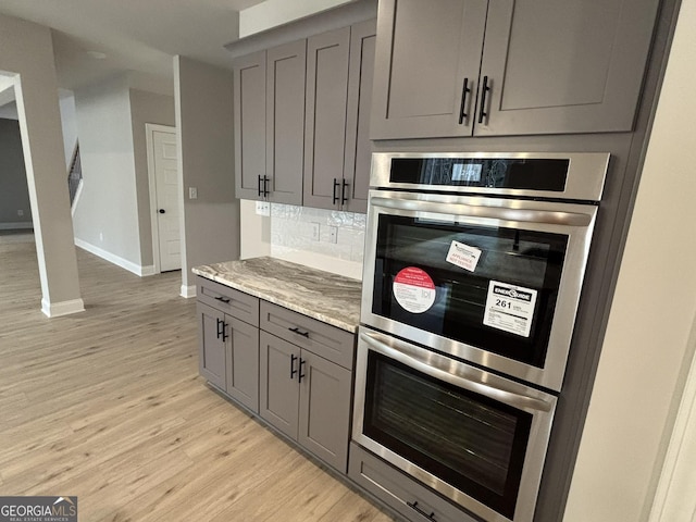 kitchen with light wood-style floors, stainless steel double oven, gray cabinets, and decorative backsplash