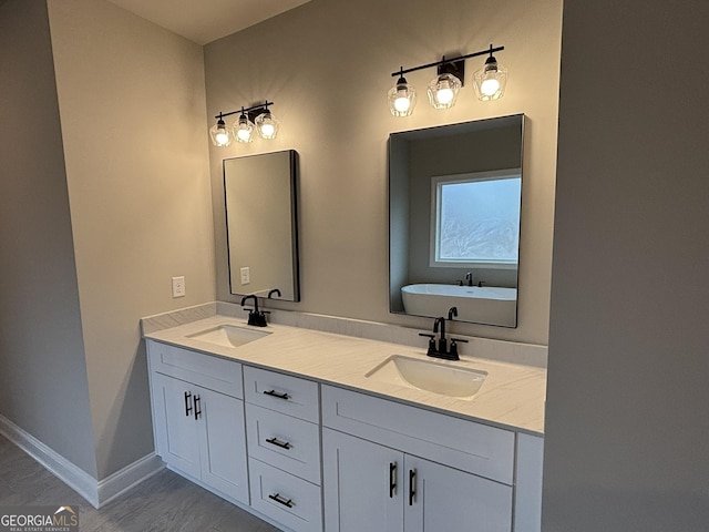 full bath featuring double vanity, a soaking tub, baseboards, and a sink