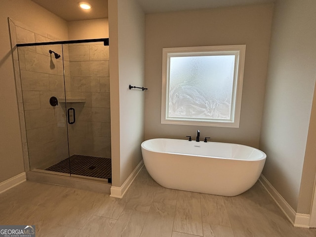 bathroom featuring a stall shower, a soaking tub, and baseboards