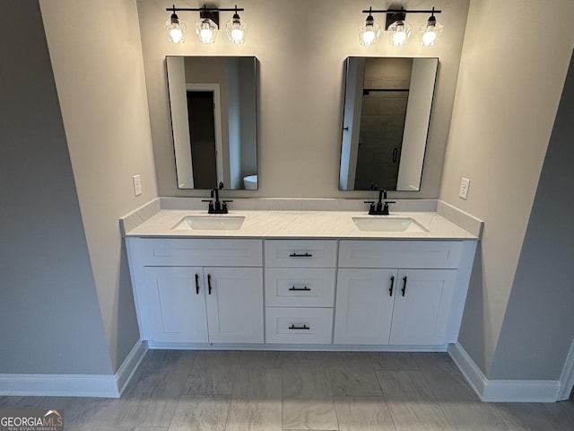 full bath featuring a stall shower, a sink, baseboards, and double vanity