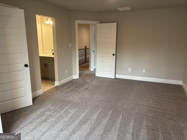 unfurnished bedroom featuring ensuite bathroom, carpet flooring, visible vents, and baseboards