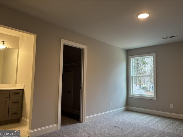 unfurnished bedroom featuring baseboards, a walk in closet, visible vents, and light colored carpet