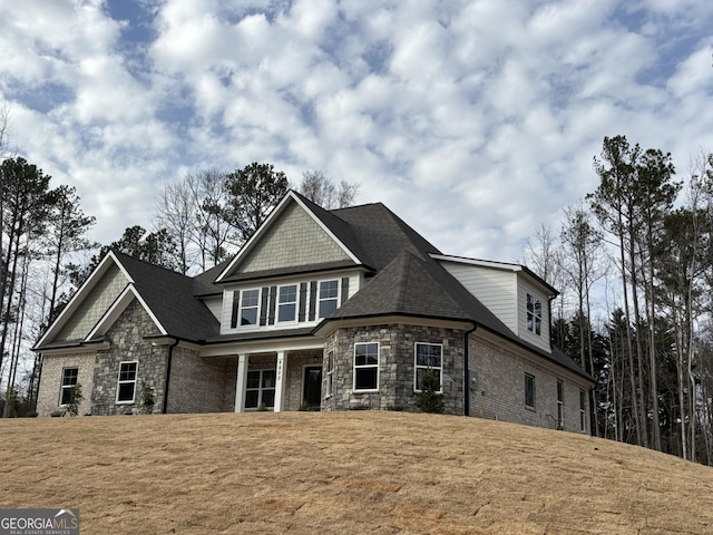 view of front of house with stone siding, roof with shingles, brick siding, and a front yard