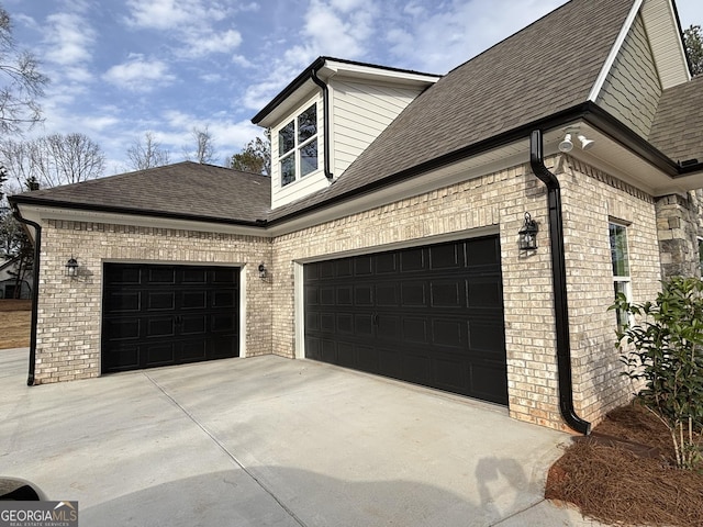 view of side of home featuring a garage, driveway, brick siding, and a shingled roof