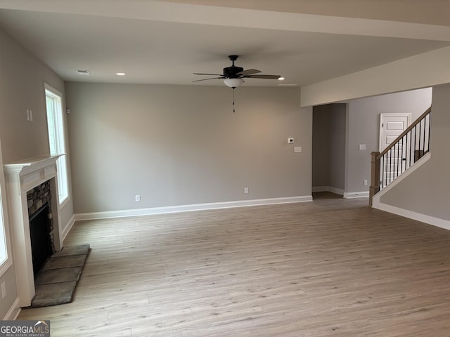 unfurnished living room with recessed lighting, a fireplace with raised hearth, light wood-style flooring, baseboards, and stairs