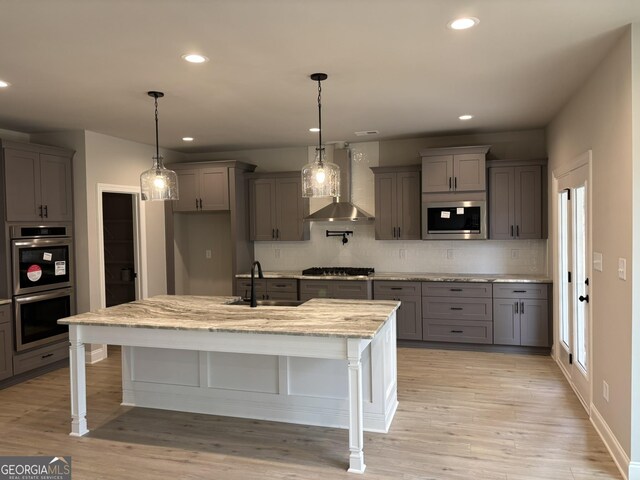 kitchen with light wood-style flooring, gray cabinetry, a sink, appliances with stainless steel finishes, and wall chimney exhaust hood