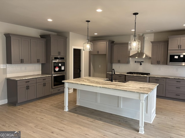 kitchen with wall chimney exhaust hood, light wood-style flooring, appliances with stainless steel finishes, gray cabinetry, and a sink