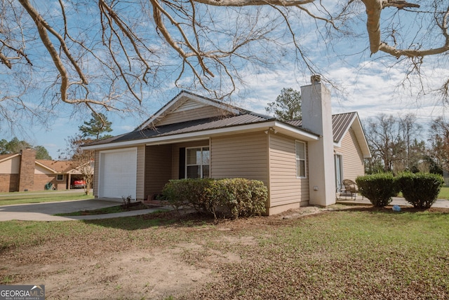 view of home's exterior with driveway, a chimney, metal roof, an attached garage, and a yard