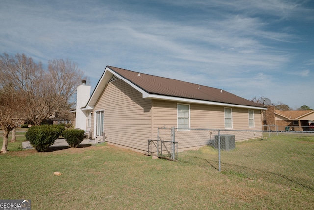 view of side of home with central air condition unit, fence, metal roof, and a yard