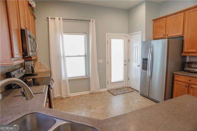 kitchen with a toaster, appliances with stainless steel finishes, brown cabinetry, and a sink