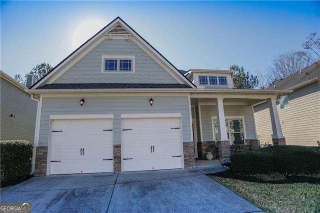 craftsman-style home featuring driveway, covered porch, an attached garage, and stone siding