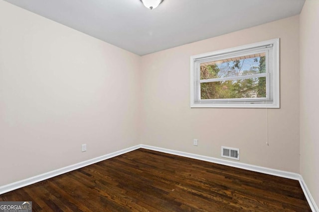 empty room featuring wood finished floors, visible vents, and baseboards