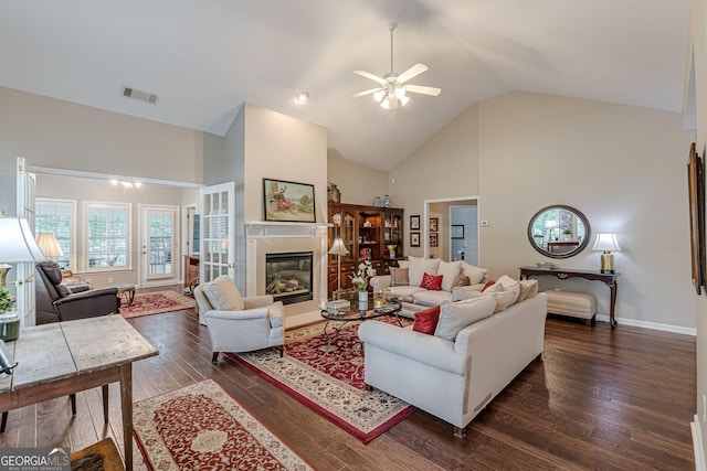 living area with high vaulted ceiling, a glass covered fireplace, visible vents, and dark wood-style floors