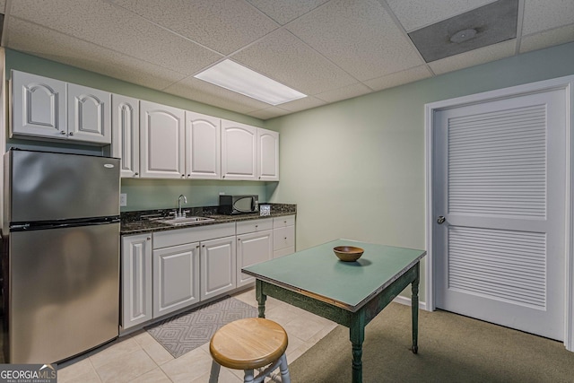 kitchen with light tile patterned floors, white cabinets, a drop ceiling, freestanding refrigerator, and a sink