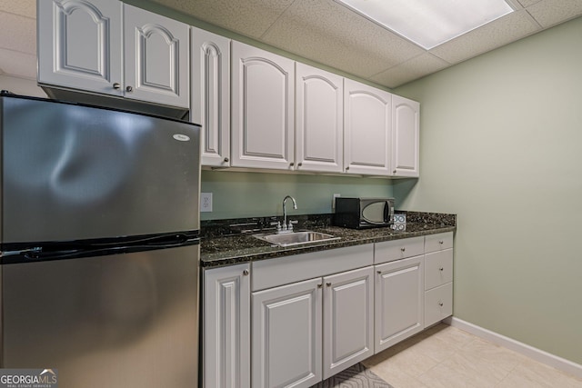 kitchen featuring black microwave, a drop ceiling, a sink, white cabinets, and freestanding refrigerator