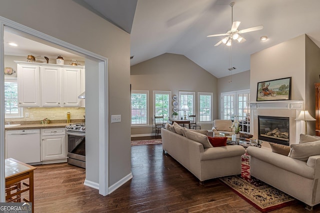 living room with baseboards, a ceiling fan, a glass covered fireplace, dark wood-type flooring, and high vaulted ceiling