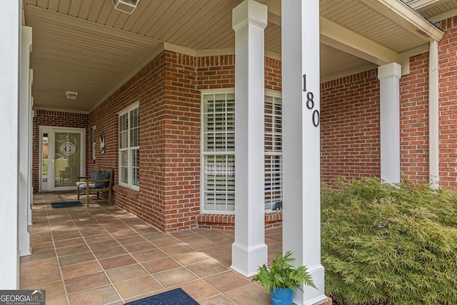 doorway to property featuring a porch and brick siding