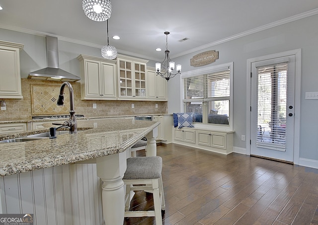 kitchen with wall chimney exhaust hood, ornamental molding, dark wood finished floors, and glass insert cabinets