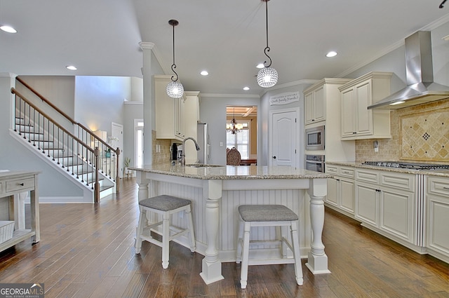 kitchen with a sink, dark wood finished floors, appliances with stainless steel finishes, wall chimney exhaust hood, and a kitchen bar