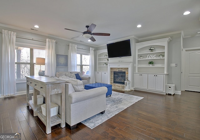 living room featuring dark wood-style floors, recessed lighting, ornamental molding, and a glass covered fireplace