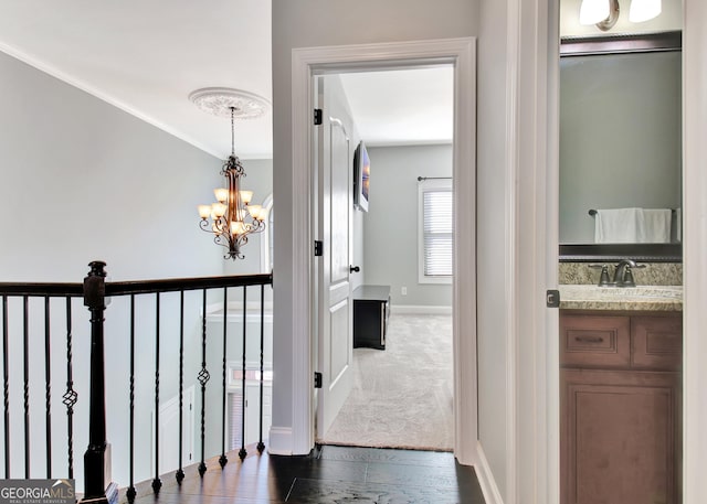 hall featuring baseboards, dark wood-type flooring, a sink, and an inviting chandelier