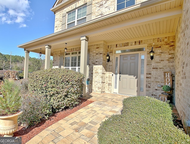 view of exterior entry featuring a porch and brick siding