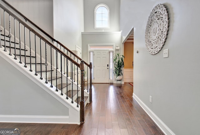 entrance foyer with a towering ceiling, baseboards, stairs, wainscoting, and dark wood finished floors